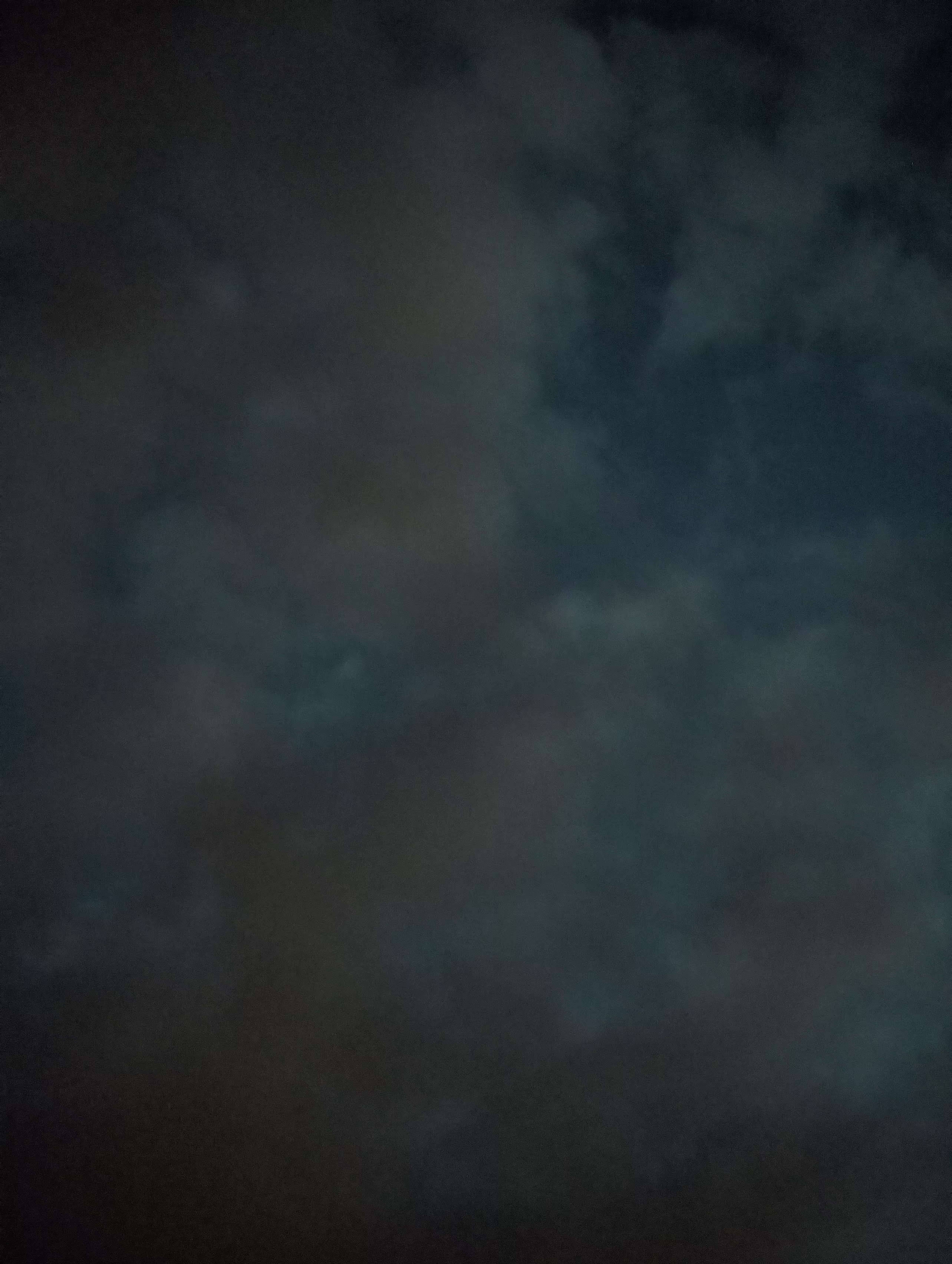 A section of the sky at night with clouds lit in greyish-yellow against a blue background
